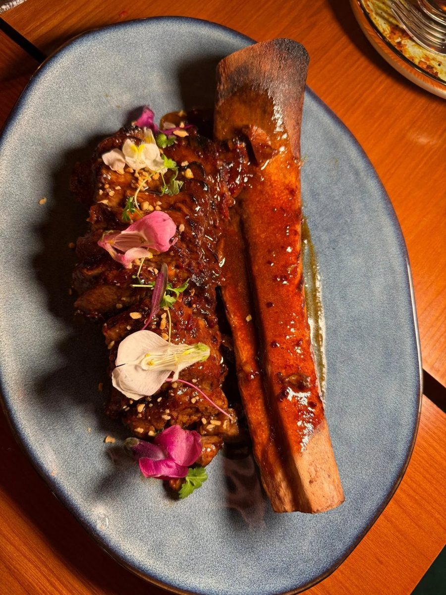 Glazed meat with a roasted marrow bone and edible flowers on a blue plate at AMATA (official photo)