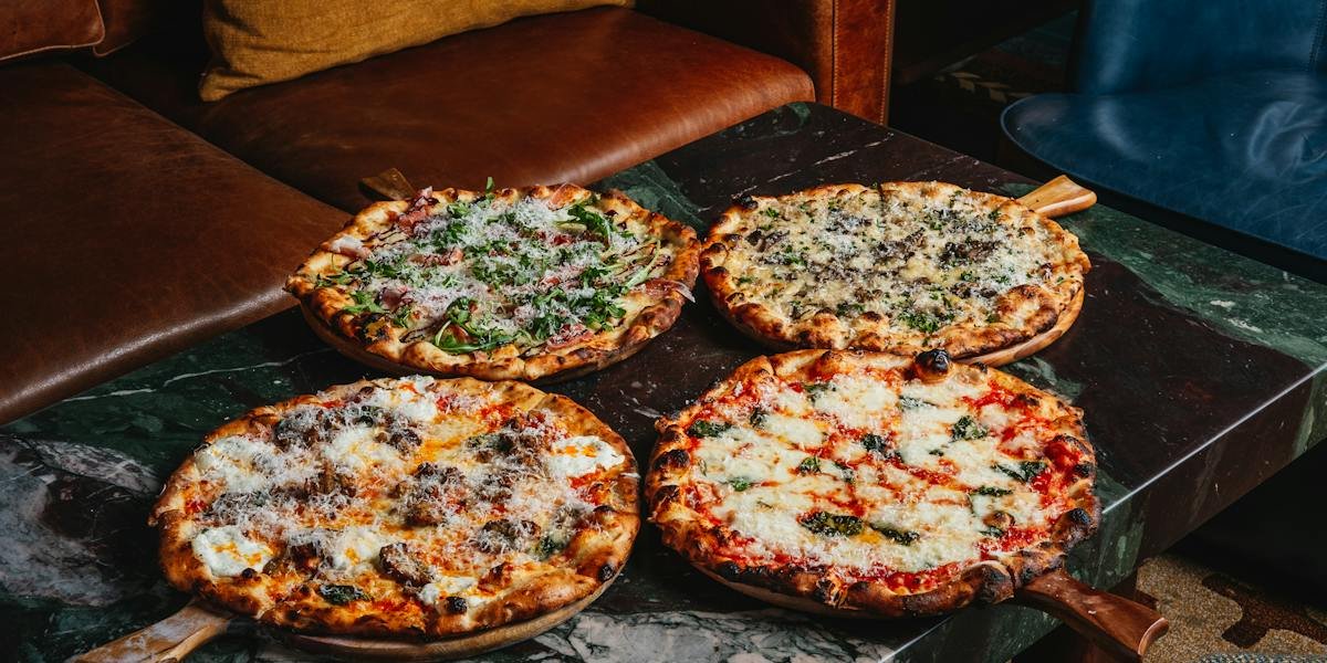 Four wood-fired pizzas on wooden peels across a green marble table at Hearthstone (official photo)