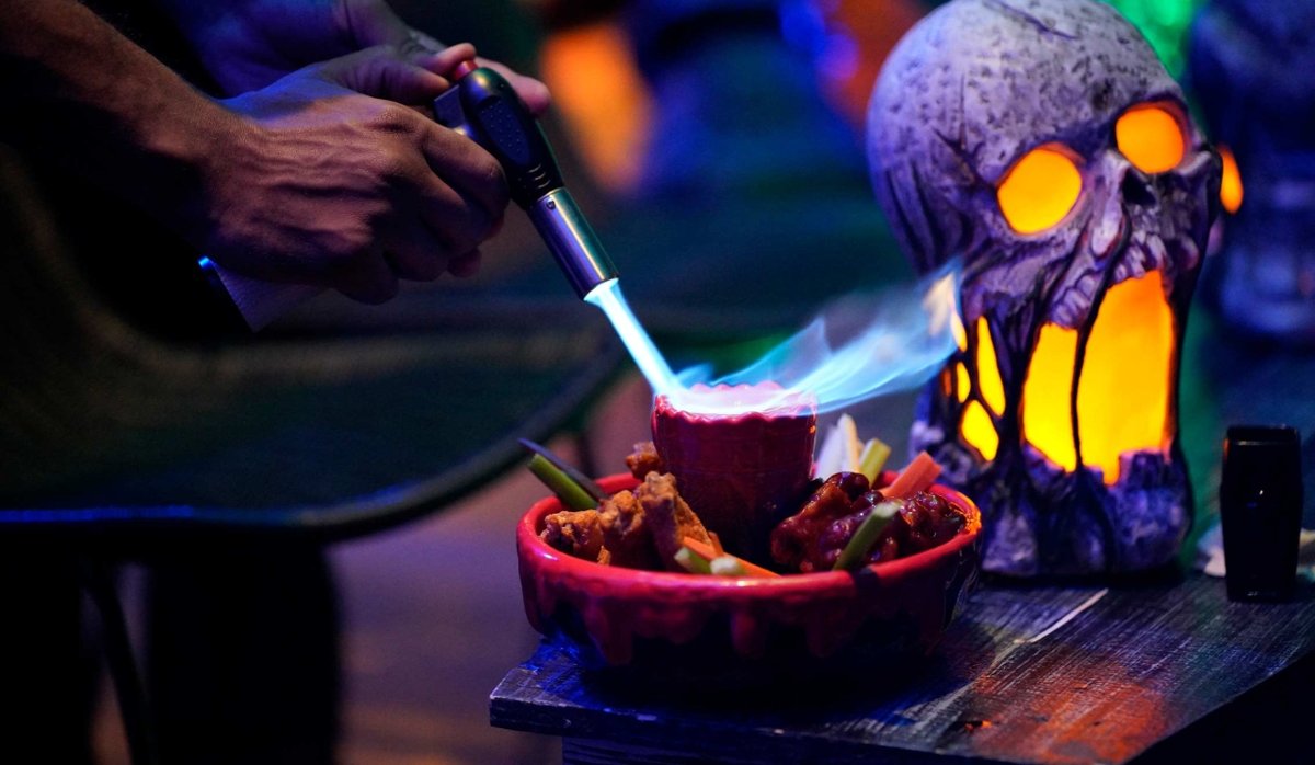 A torch flames a bowl of wings with celery next to a glowing skull lantern at The Haunted Inn (official photo)