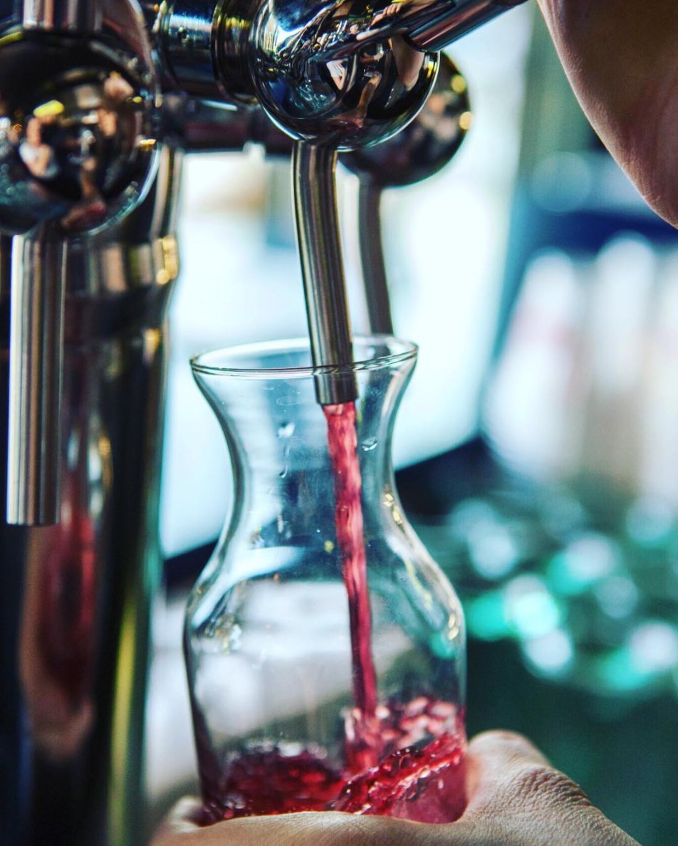 Red wine pouring from a tap into a glass carafe at Bin 702 (official photo)