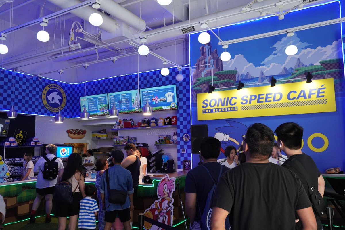 Guests line up inside a previous Sonic Speed Café pop-up under a yellow sign and blue checkered walls