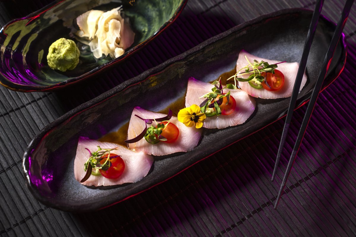 Slices of yellowtail sashimi with garnish on a dark plate at Morimoto (MGM Resorts photo)
