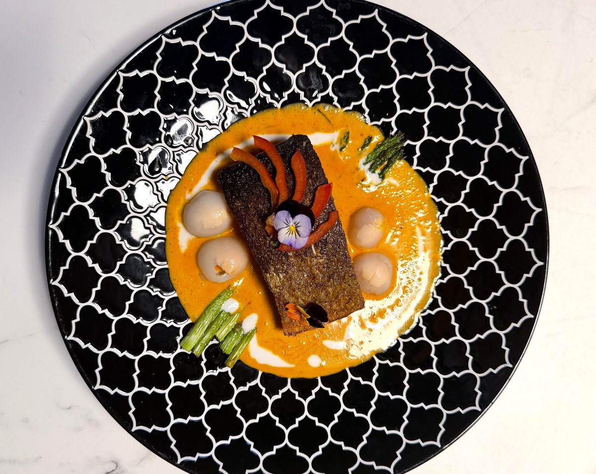 Crispy-skin salmon in orange Panang curry with lychees and asparagus on a black patterned plate at Blue Orchid Thai Kitchen (venue photo)