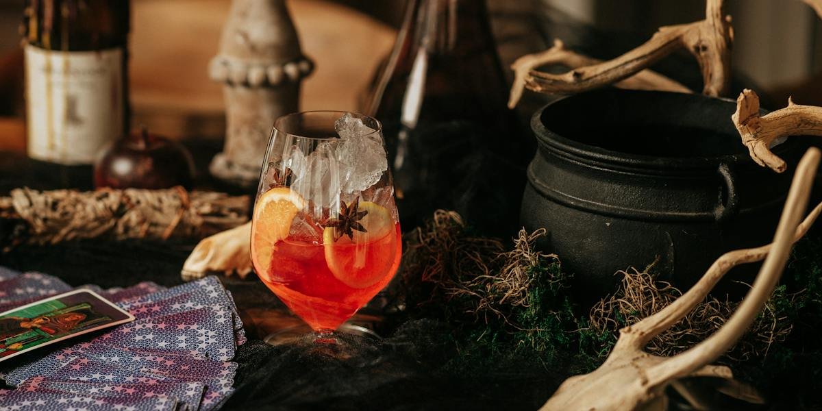 Red-orange cocktail with orange slices and star anise next to tarot cards, a black cauldron and driftwood (La Strega photo)