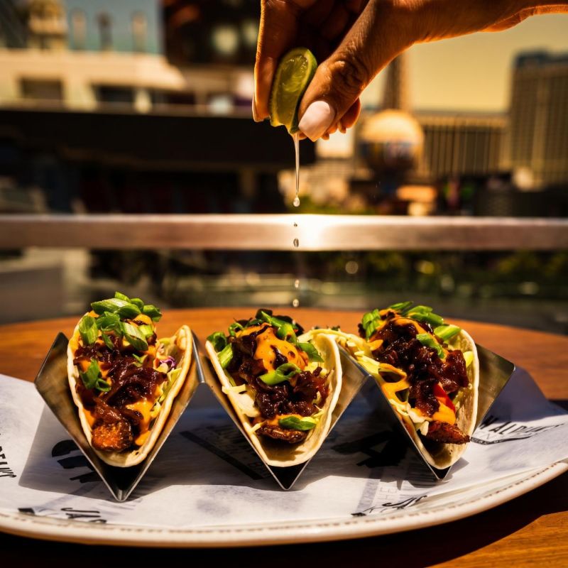 Three blackened salmon tacos on a plate with lime being squeezed over them and the Strip in the background (venue photo)