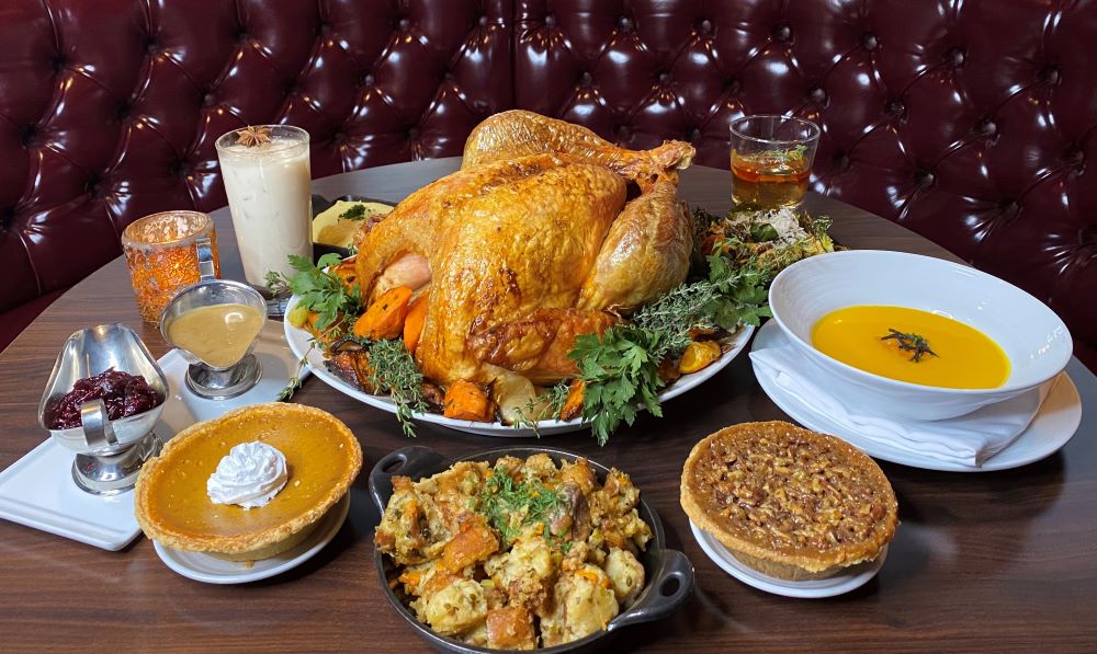 Thanksgiving spread at Oscar's with a roast turkey, butternut squash soup, stuffing and two pies on a table in a red leather booth (venue photo)