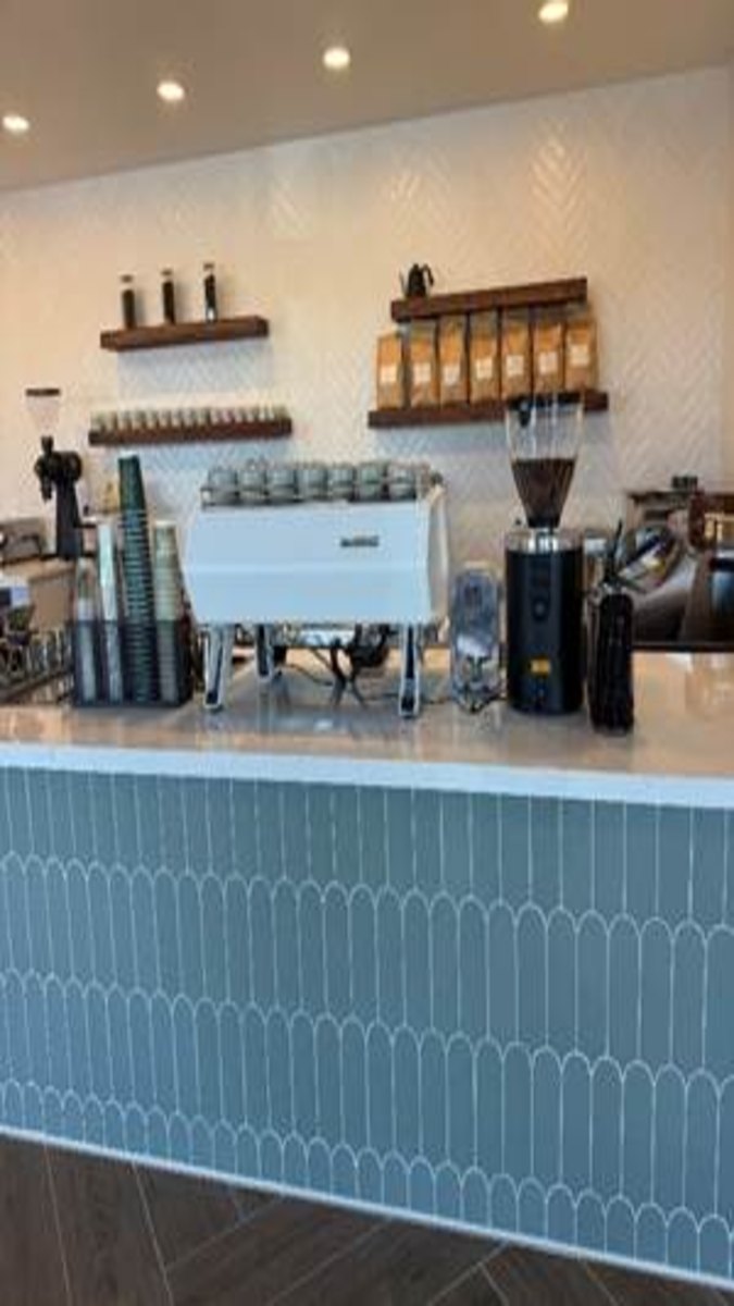 Almond & Oat's espresso bar with a white espresso machine, grinders and wood shelves of coffee (Almond & Oat photo)