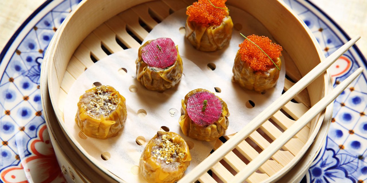 Dumplings with colorful toppings in a bamboo steamer on a patterned plate (China Poblano photo)