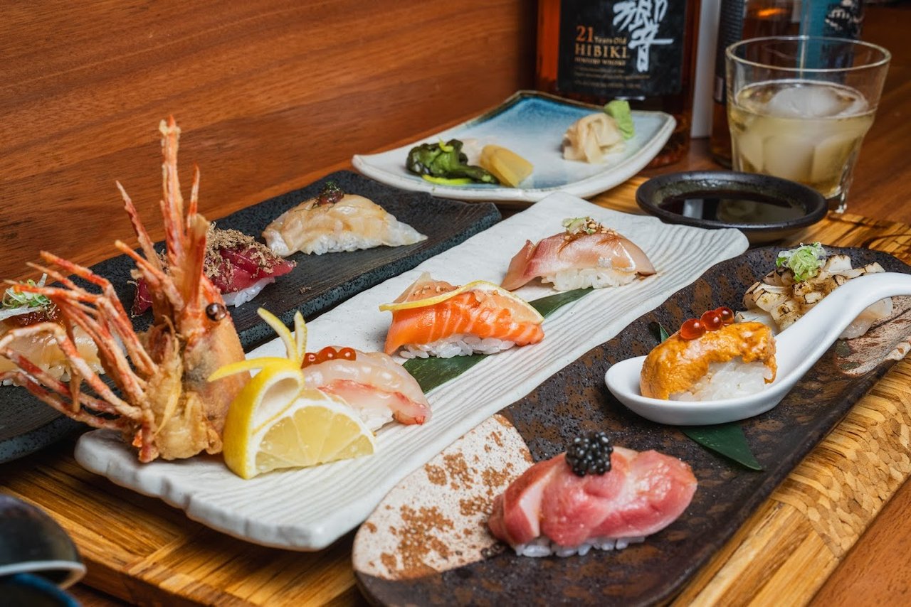 Wooden boards of nigiri, sashimi and a whole grilled shrimp on a sushi bar counter (Omakase Kyara photo)