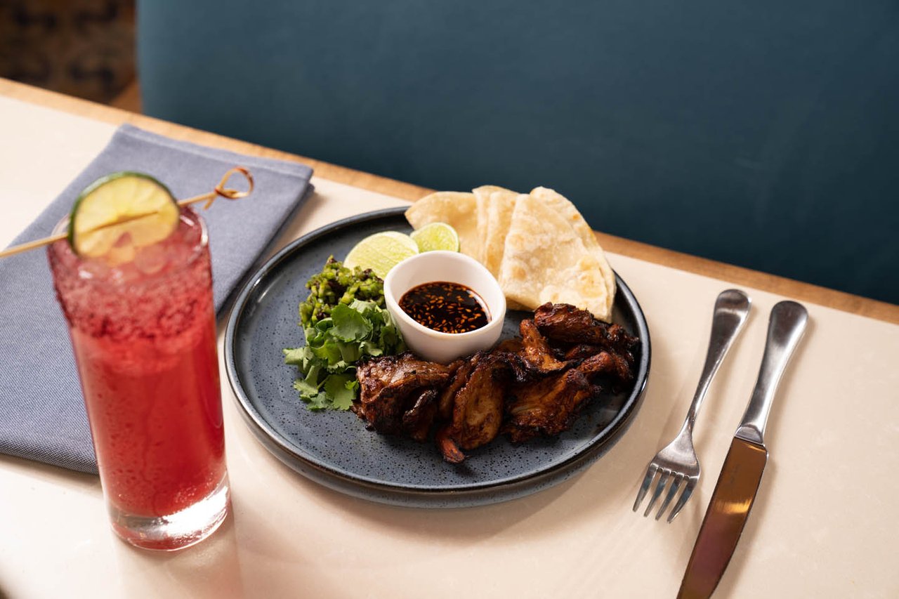 A plate of grilled meat with flour tortillas, salsa and greens next to a red agua fresca with a lime wheel (Resorts World photo)