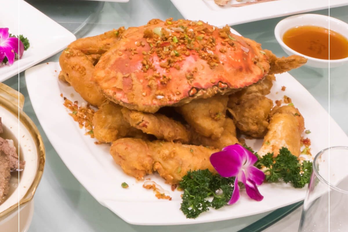 A whole salt and pepper crab with fried crab pieces on a white platter, garnished with parsley and an orchid (R&G Lounge photo)
