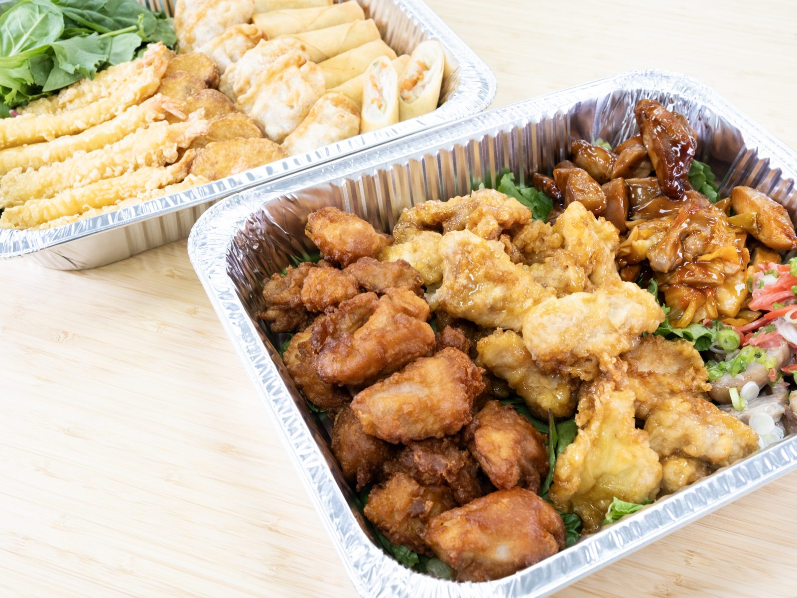 Two foil catering trays, one of fried chicken and teriyaki chicken, the other of shrimp tempura, gyoza and spring rolls (J Gourmet Market photo)
