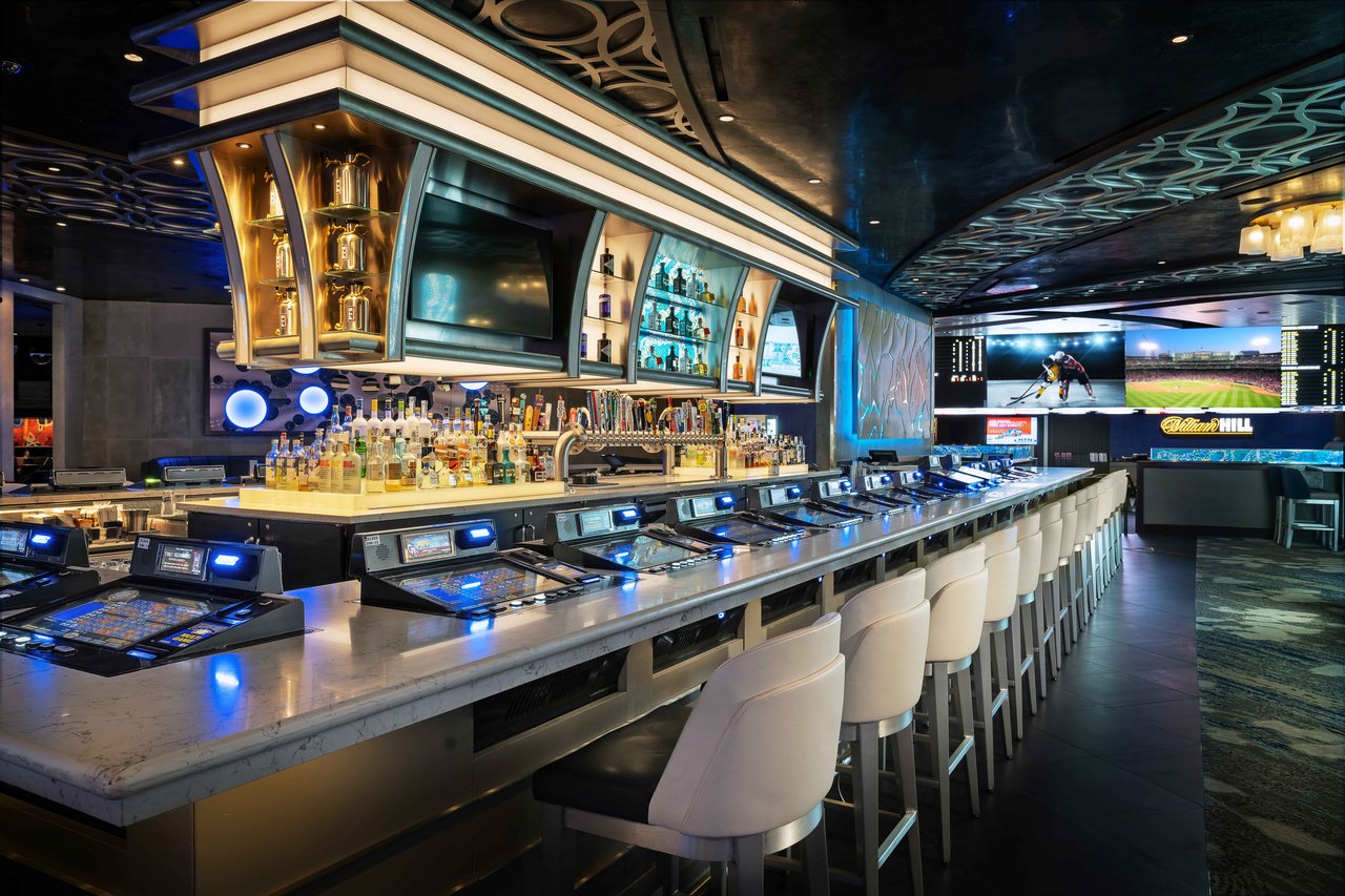 The long View Lounge bar at The STRAT with white stools, bar-top games and sportsbook screens (The STRAT photo)