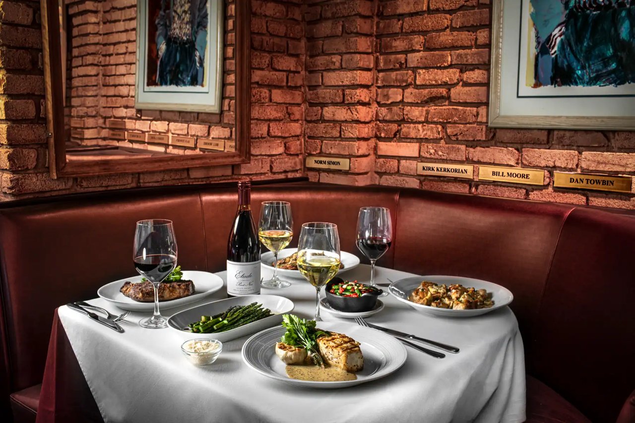 A red leather booth and a white-tablecloth table set with plates and wine glasses under framed art at Piero's (Piero's photo)