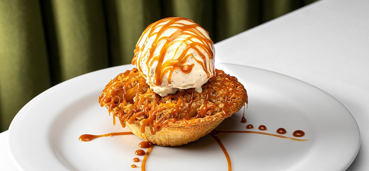 An apple crumble dessert topped with vanilla ice cream and caramel on a white plate at Alex Prime (El Cortez photo)