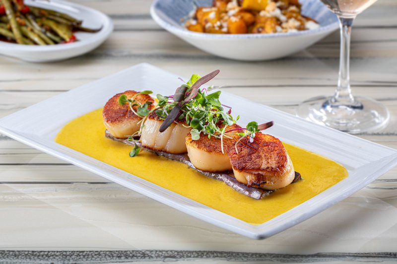 Seared scallops on a bright yellow sauce with side dishes behind them at Top of the World (The STRAT photo)